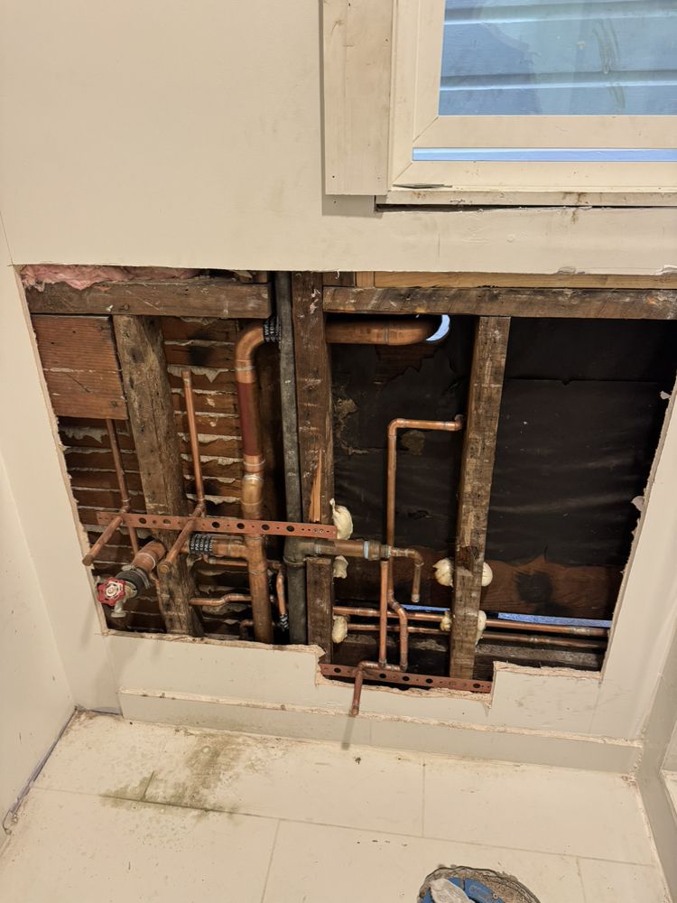 Open bathroom wall showing organized copper plumbing lines during a repair